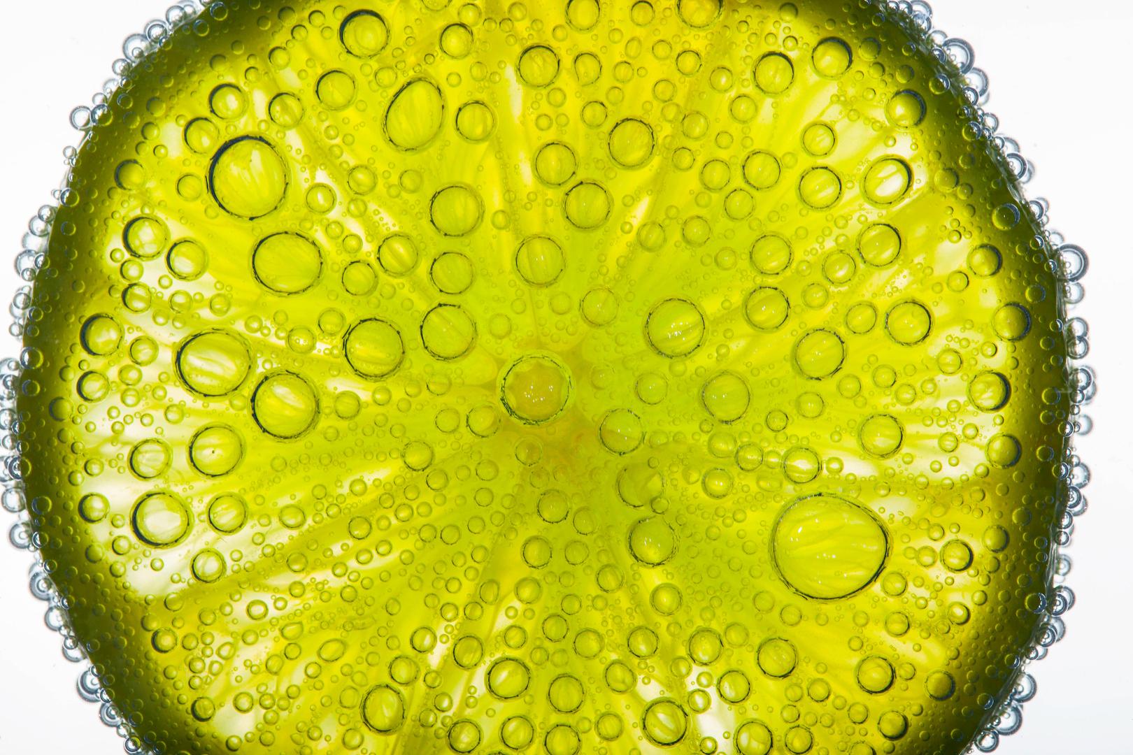 Close-up of air bubbles covering slice of juicy lime floating in